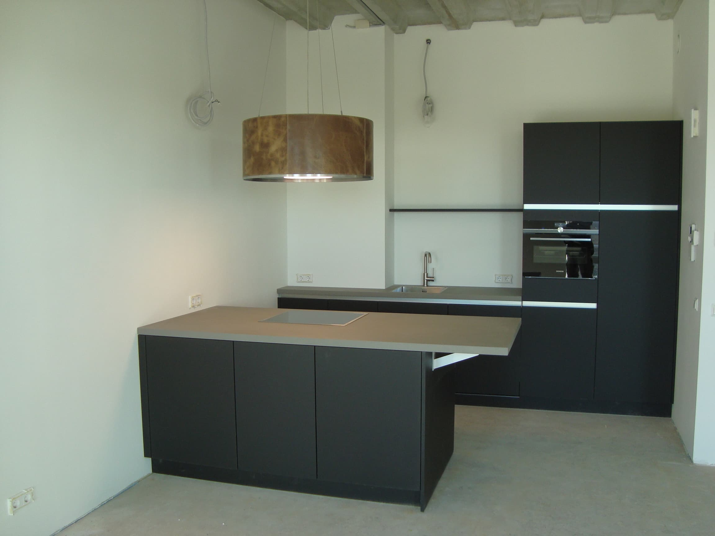 Door HKT geplaatste matzwarte keuken met kookeiland en koperen hanglamp